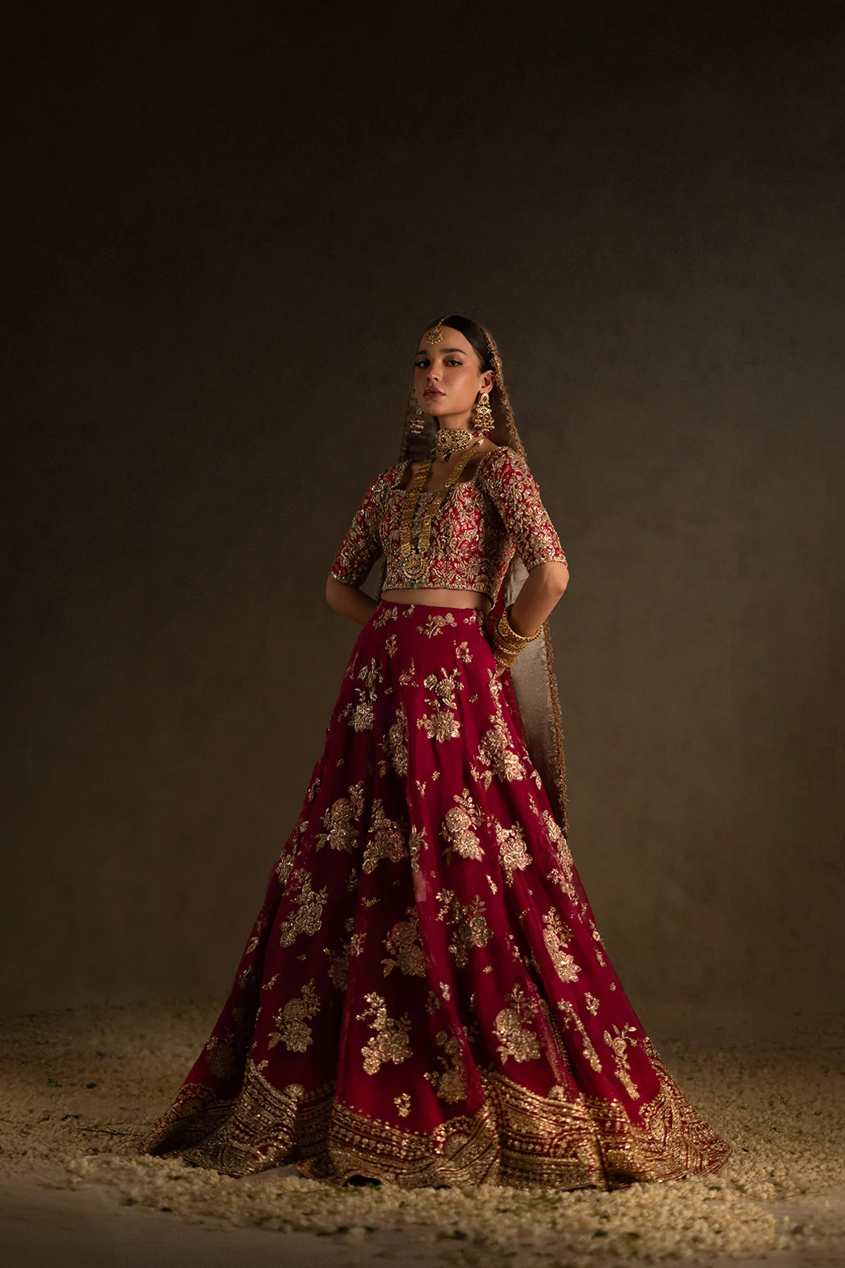 A marsala pink bridal ensemble featuring a hand-embroidered choli, adorned with delicate pastel tones, intricate zardozi, and sequin work. The printed lehenga boasts a heavily embellished gotta and zardozi border at the hem, complemented by intricately embellished motifs throughout.
